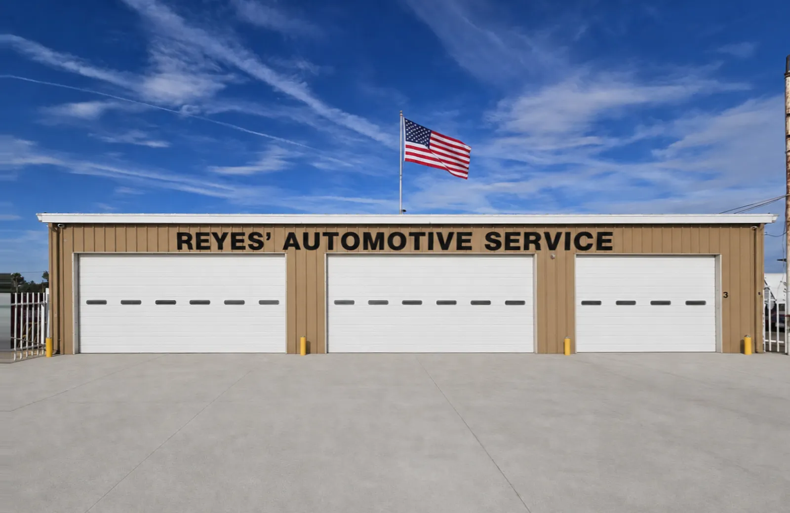 Front of Reyes' Automotive Service in Delano with three garage bays and an American flag